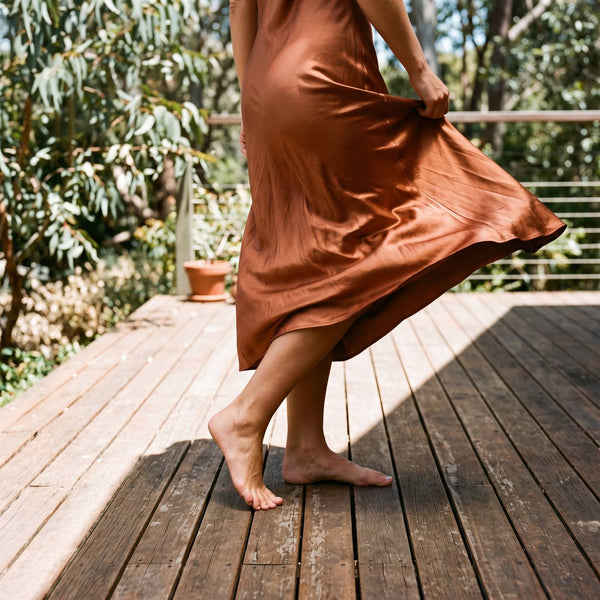 Close crop of a copper satin slip dress swirling on sunlit timber decking