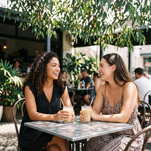 Two friends in summer dresses at an outdoor cafe table in dappled sunlight